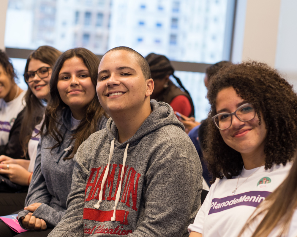 4 people appear in the picture; they are sitting down. a boy sitting in the middle among other girls and they all smile and facing straight on the picture