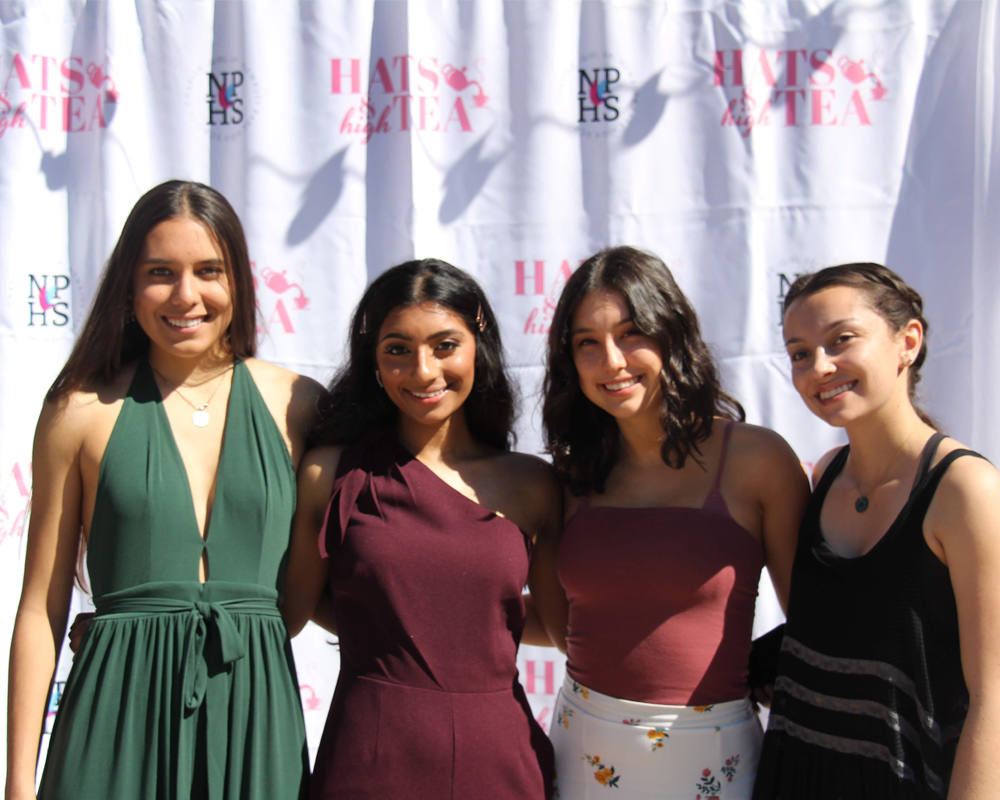 (upper body shot) 4 girls have their hand around each other shoulder and pose for the picture at a hats high tea and NPHS event