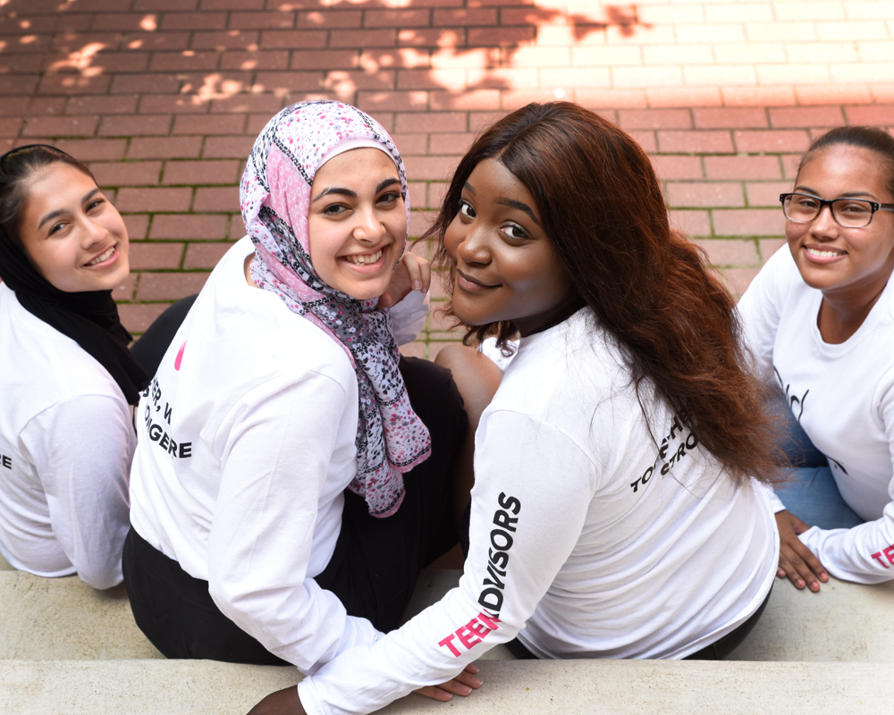 4 teen advisors are sitting on the stairs and looking back to facing up for the picture.