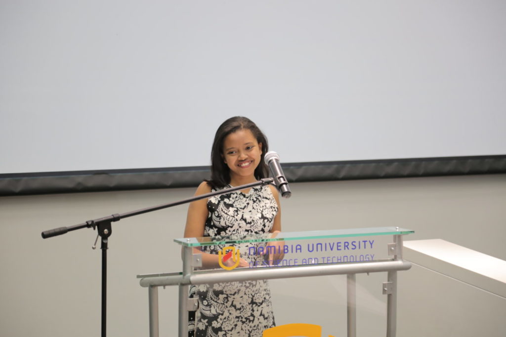 Beza is speaking in front of the Podium and with her big smile on her face