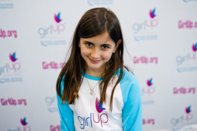 Darya Pishevar_The founding class of Teen Advisors(close angle, but not clear picture headshot ) a teen girl wearing her girl up blue long shirt with her smiley face looking down a little bit facing the camera, and background is girlup.org board