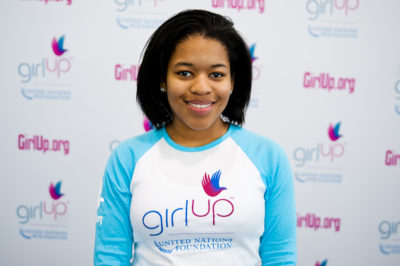 Erica Lamberson_The founding class of Teen Advisors(close angle, but not clear picture headshot ) a teen girl wearing her girl up blue long shirt with her smiley face facing the camera, and background is girlup.org board
