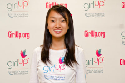 Eva (YingYing) Shang_2012-2013 Class Teen Advisors (close angle headshot, a little blurry picture ) a teen girl wearing her girl up white shirt with her smiley face facing the camera, and background is girlup.org board