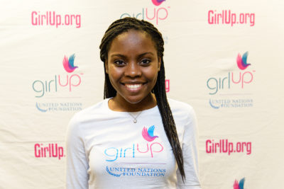 Gloria Samen_2013-2014 Teen Advisor (close angle headshot, a picture little blurry ) a teen girl wearing her girl up white shirt with her smiley face facing the camera, and background is girlup.org board