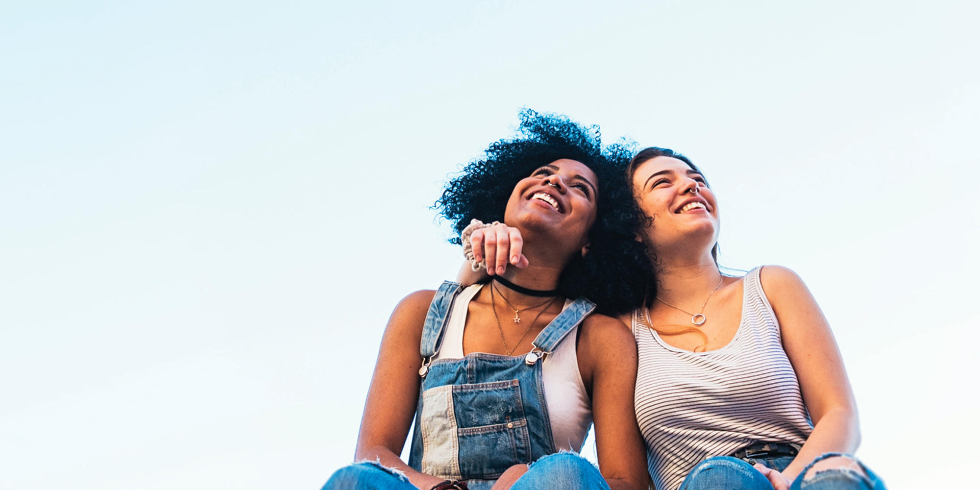 two girls looking at the sky and smile, one girl has her arm around the other girl's shoulder (lower angle)