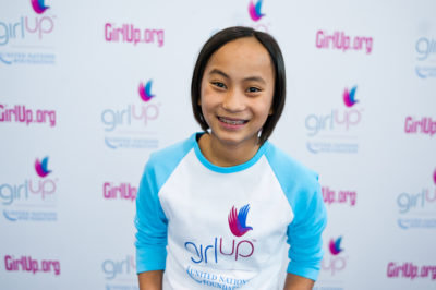 Isabella Solimene,The founding class of Teen Advisors(close angle, but not clear picture headshot ) a teen girl wearing her girl up blue long shirt with her smiley face facing the camera, and background is girlup.org board