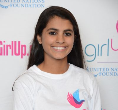 Ishana Nigam_ 2014-2015 Teen Advisors (close angle headshot) a teen girl wearing her girl up white shirt with her smiley face facing the camera, and background is girlup.org board