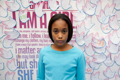 Jillian Medina,The founding class of Teen Advisors(close angle, but not clear picture headshot ) a teen girl wearing her girl up blue long shirt facing the camera, and background is girlup.org board