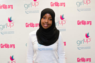 Munira Khalif, Hometown: Fridley, MN_2012-2013 Class Teen Advisors (close angle headshot, a little blurry picture ) a teen girl wearing her girl up white shirt with her smiley face facing the camera, and background is girlup.org board