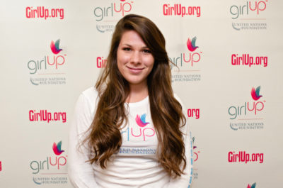 Natasha Madorsky, Hometown: Cleveland, OH_2012-2013 Class Teen Advisors (close angle headshot, a little blurry picture ) a teen girl wearing her girl up white shirt with her smiley face facing the camera, and background is girlup.org board