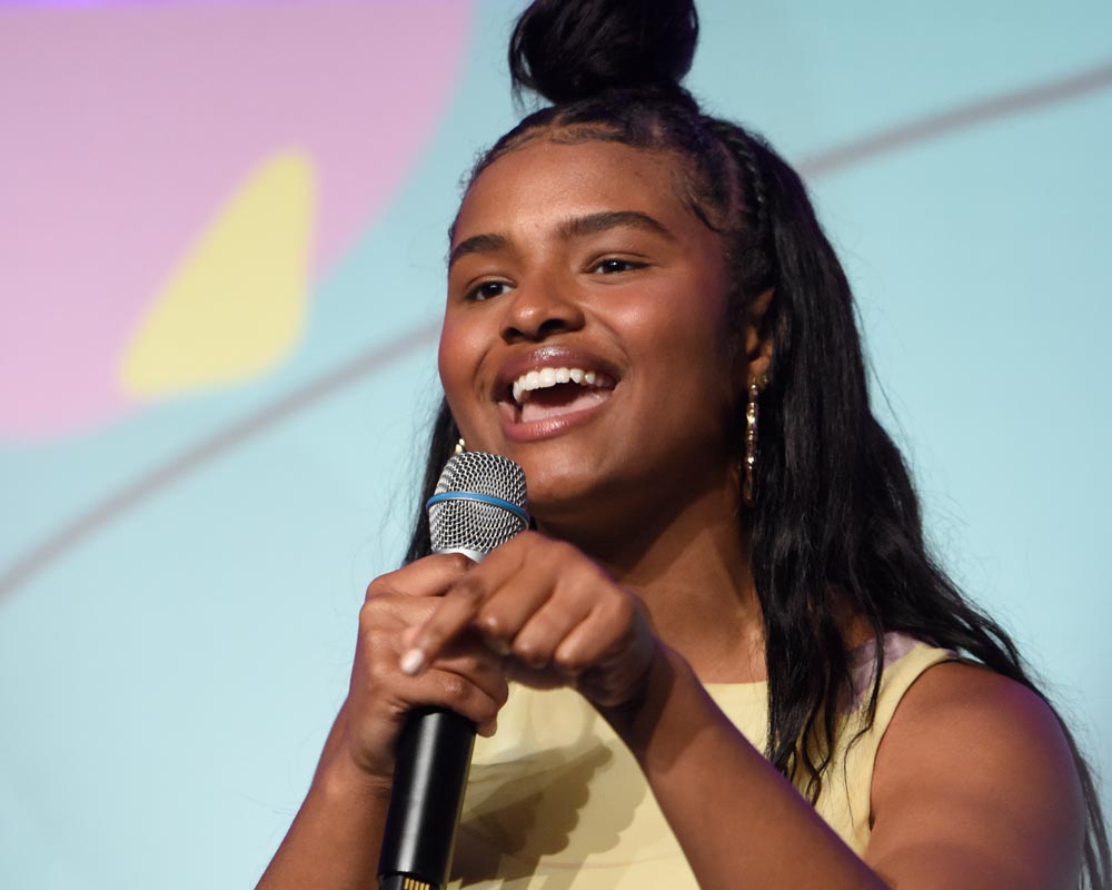 (close head shot)a girl is holding a mic on her right hand and her left hand finger point down and speaking