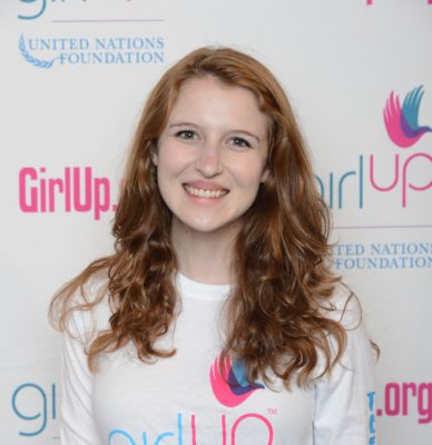 Sarah Gordon 2013-2014 Teen Advisor (close angle headshot, a picture little blurry ) a teen girl wearing her girl up white shirt with her smiley face facing the camera, and background is girlup.org board