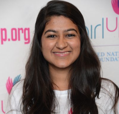 Sarah Khimjee_ 2014-2015 Teen Advisors (close angle headshot ) a teen girl wearing her girl up white shirt with her smiley face facing the camera, and background is girlup.org board