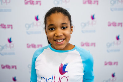 Sydney Medina, The founding class of Teen Advisors(close angle, but not clear picture headshot ) a teen girl wearing her girl up blue long shirt with her smiley face facing the camera, and background is girlup.org board