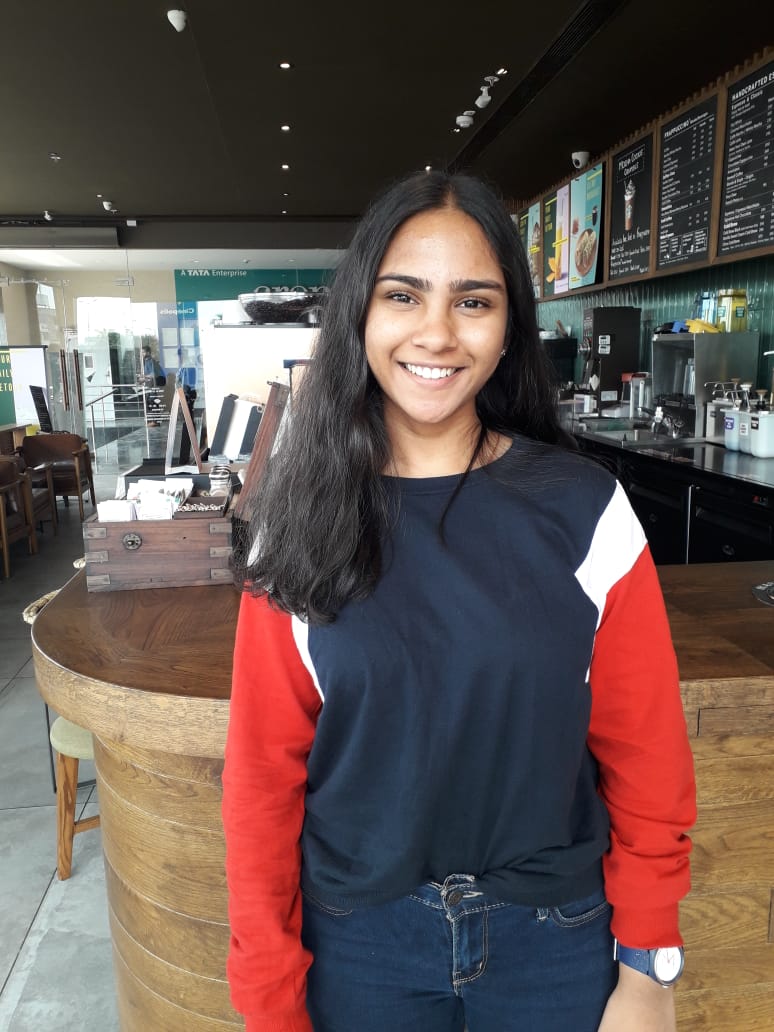 Tanushah Ramadass 2019-2020 Teen Advisors (half body headshot) with her smiley face facing to the camera , background is coffee shop