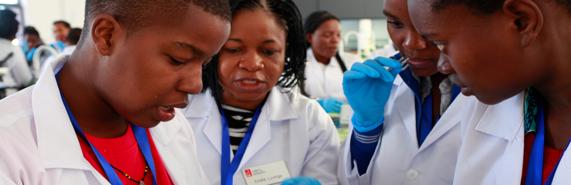 a girl of teens with white coast on and holding on the experiment and looking at the teacher and listen to her explanation