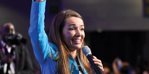 Julie Carrier is speaking with a mic on her left and she is rising her right hand up