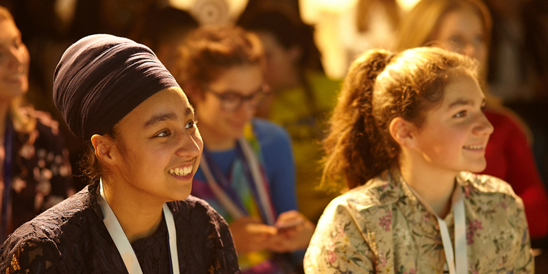 two Girl Up members in Europe from different ethnic backgrounds smiling and together at the event listening to the speaker (close shot)
