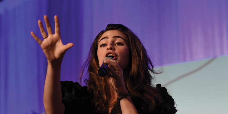 lower angle shot _ a girl holding a mic and have right hand open face toward to the front