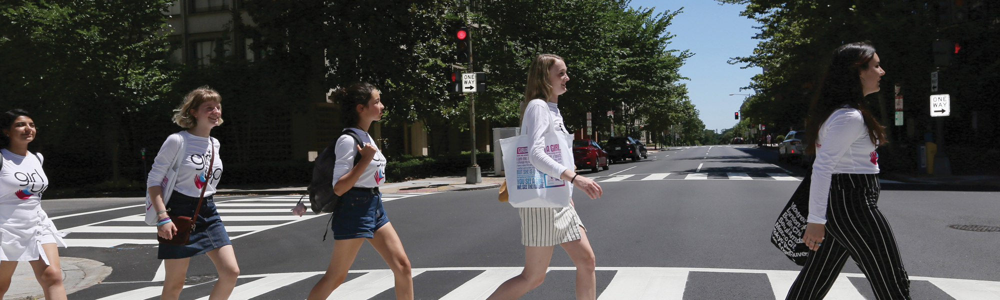 5 girls cross street one after other facing forward with their teen adviser shirt on