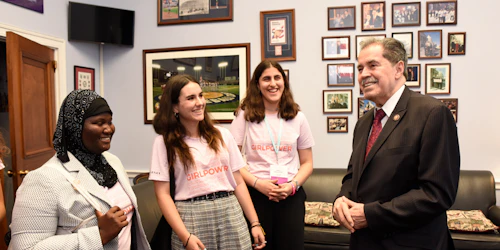 3 Girl Up members (wearing girl power t-shirt) smile and talking with an official