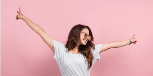 a girl with two of her arm wide open posing victory sign and big smile with pink background